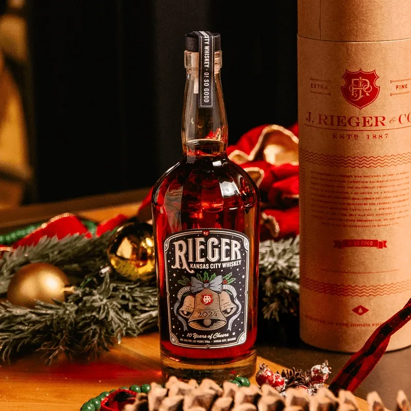 J. Rieger 2024 Holiday Whiskey label — complete nighttime composition featuring hand-drawn silver foil bells, holly leaves, ornate typography, and three historic dates representing the brand's legacy from pre-Prohibition to present